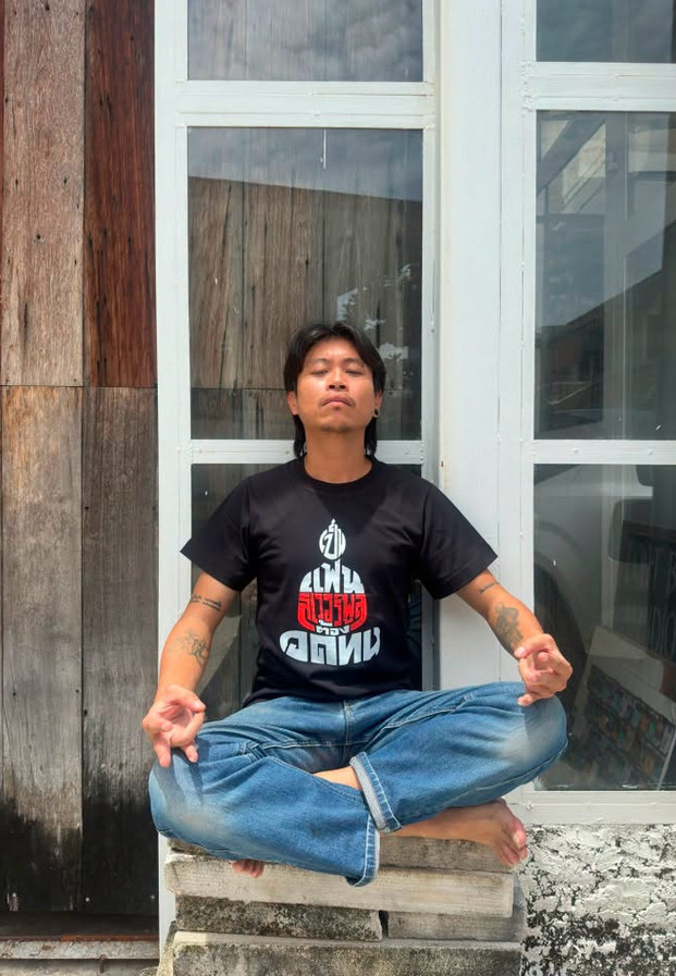 ลิขิต สิทธิพันธุ์ นั่งขัดสมาธิหน้าอาคารไม้