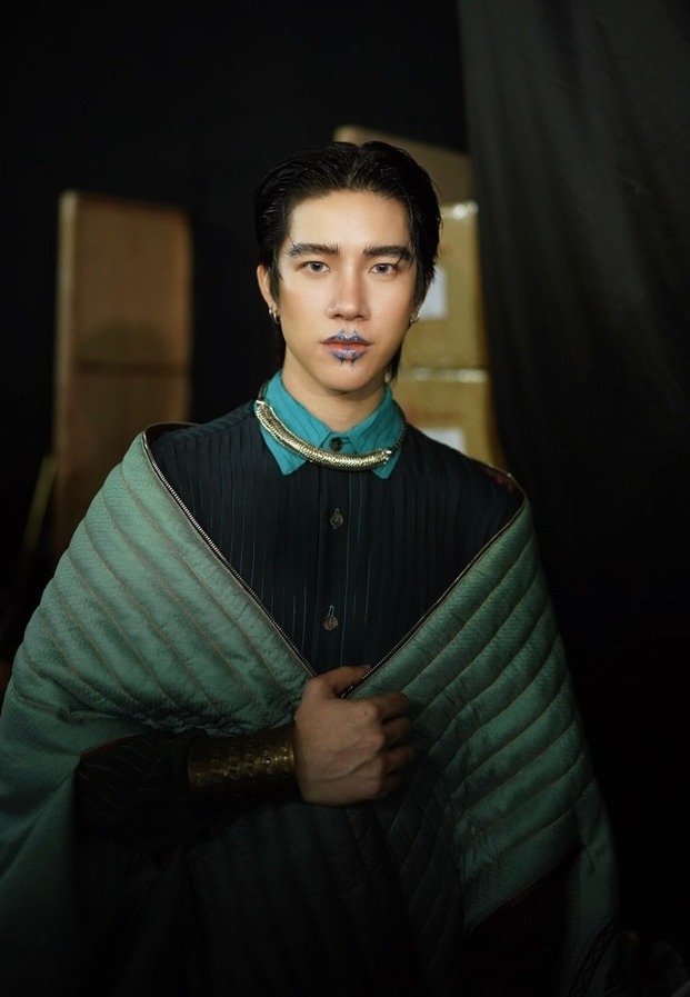 แฟรงค์ในชุดแฟชั่นโทนสีเขียวเข้มและเทาพร้อมเครื่องประดับคอสีทอง