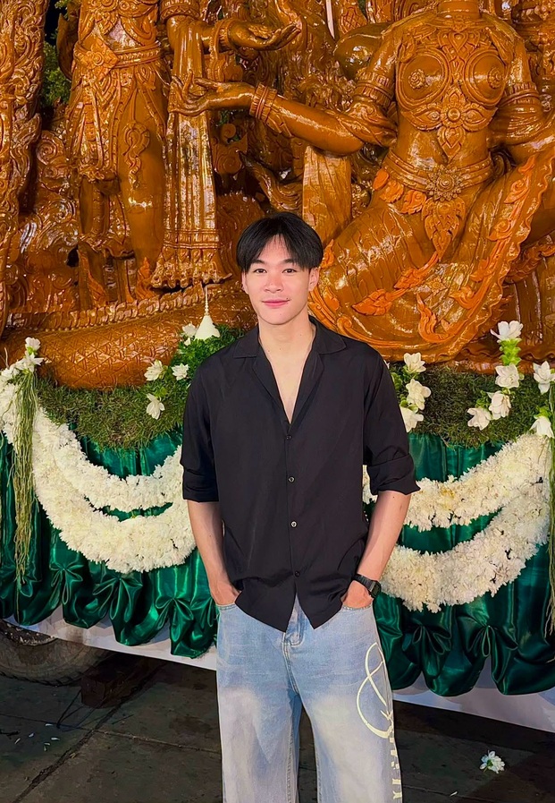 มอสในเสื้อเชิ้ตดำยืนหน้างานแกะสลักสีส้มทอง